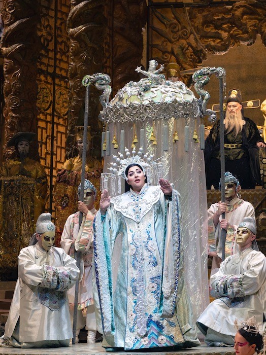 Christine Goerke in blue gown surrounded by servants singing the role of Turandot.